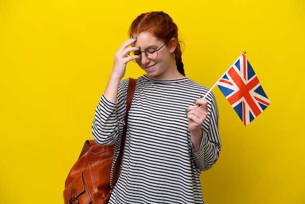 Jonge Spaanse vrouw met een vlag van het Verenigd Koninkrijk geïsoleerd op gele achtergrond lachen