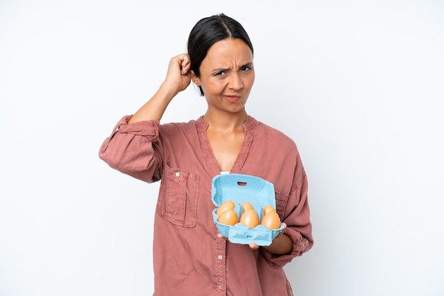 Jonge spaanse vrouw met eieren geïsoleerd op een witte achtergrond met twijfels