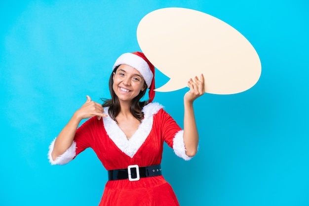 Jonge spaanse vrouw verkleed als mama noel geïsoleerd op blauwe achtergrond met een lege tekstballon en telefoongebaar