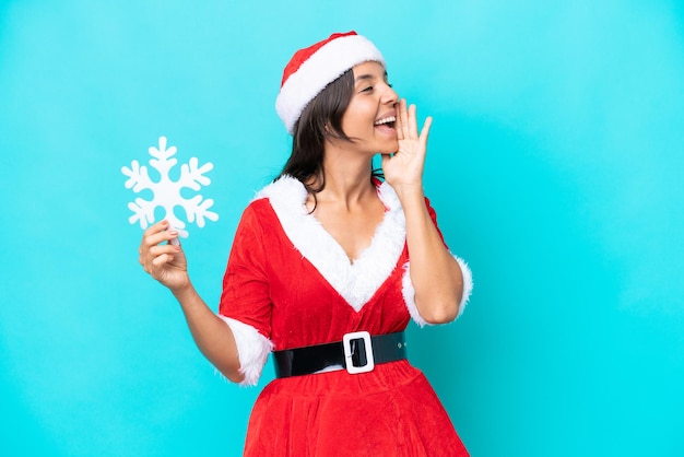 Jonge Spaanse vrouw verkleed als mama noel met een sneeuwvlok geïsoleerd op blauwe achtergrond schreeuwend met de mond wijd open naar de zijkant