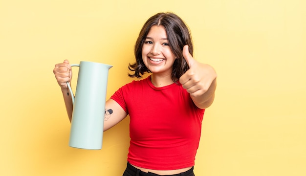 Jonge spaanse vrouw voelt zich trots, positief glimlachend met duimen omhoog. thermos concept