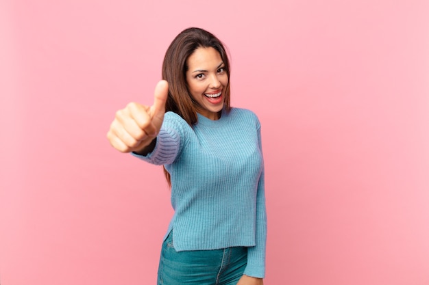 Jonge Spaanse vrouw voelt zich trots, positief glimlachend met duimen omhoog