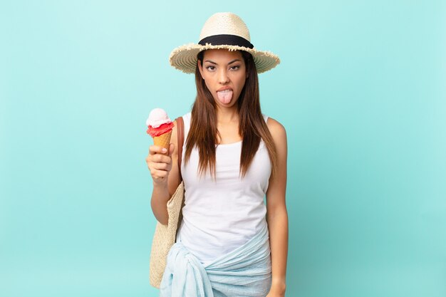 Jonge spaanse vrouw voelt zich walgelijk en geïrriteerd en tong uit en houdt een ijsje vast. zomer concept