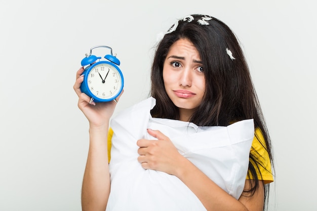 Jonge Spaanse vrouw wakker met een kussen en een wekker