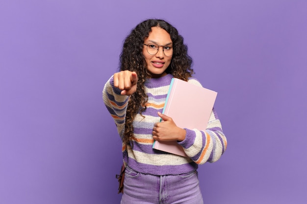 Jonge spaanse vrouw wijzend op camera met een tevreden, zelfverzekerde, vriendelijke glimlach, jou kiezen. studentenconcept