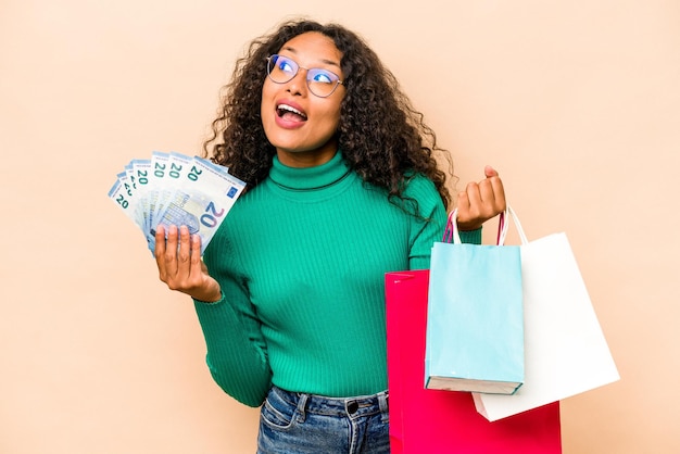 Jonge Spaanse vrouw winkelen en houden van bankbiljetten geïsoleerd op beige background