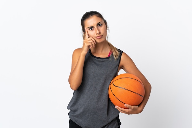 Jonge Spaanse vrouwen speelbasketbal over geïsoleerde witte muur die een idee denken