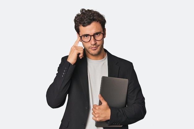Jonge Spaanse zakenman met laptop die naar de tempel wijst met vingers die op een taak denken