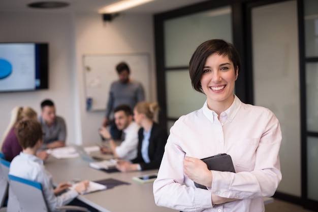 jonge Spaanse zakenvrouw portret met tabletcomputer bij moderne startup business office interieur, mensengroep op teamvergadering blured op achtergrond