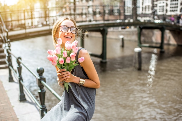 Jonge speelse vrouw zit met een boeket roze tulpen in de buurt van het waterkanaal in de stad Amsterdam