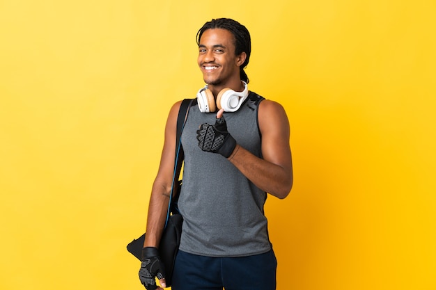 Jonge sport African American man met vlechten met zak geïsoleerd op gele achtergrond met een duim omhoog gebaar