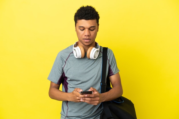 Jonge sport Afro-Amerikaanse man met sporttas geïsoleerd op gele achtergrond die een bericht verzendt met de mobiel