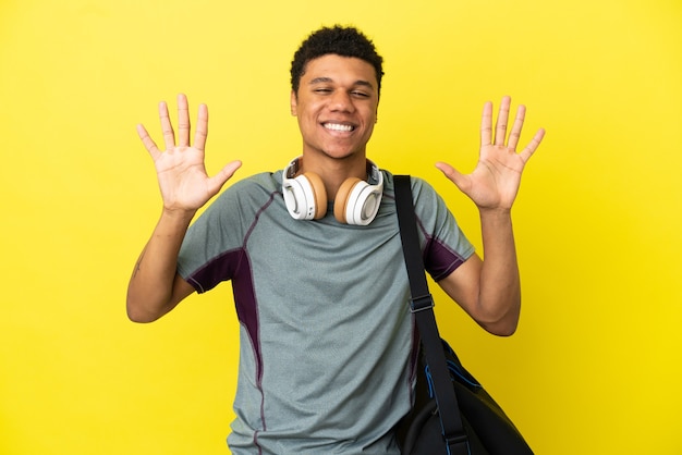 Jonge sport Afro-Amerikaanse man met sporttas geïsoleerd op gele achtergrond die tien telt met vingers