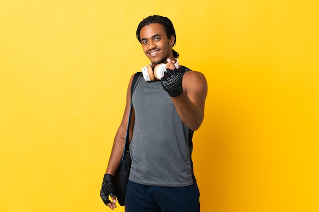 Jonge sport Afro-Amerikaanse man met vlechten met zak geïsoleerd op gele muur geld gebaar maken