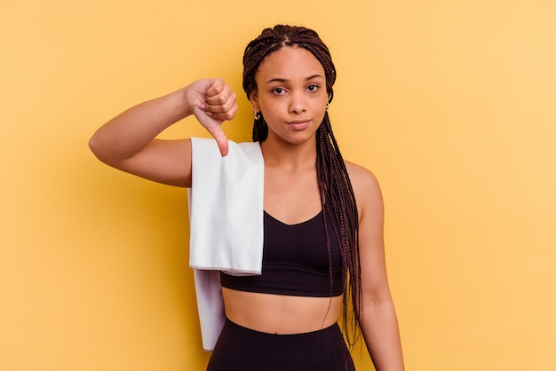 Jonge sport Afro-Amerikaanse vrouw met een handdoek geïsoleerd op gele achtergrond met een afkeer gebaar, duimen naar beneden. Meningsverschil concept.