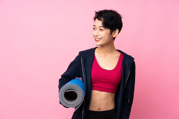 Jonge sport Aziatische vrouw over geïsoleerde roze muur met een mat en het glimlachen