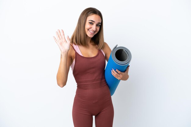 Jonge sport blanke vrouw die naar yogalessen gaat geïsoleerd op een witte achtergrond saluerend met de hand met gelukkige uitdrukking