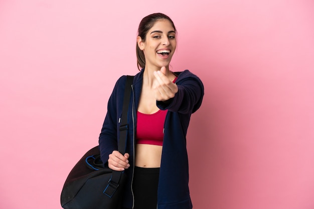 Jonge sport blanke vrouw met sporttas geïsoleerd op roze achtergrond geld gebaar maken