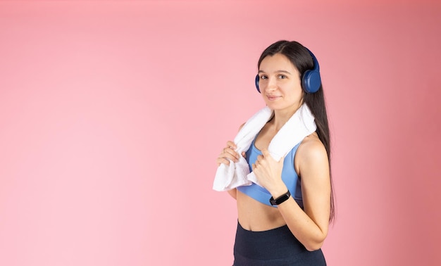 Jonge sport brunette vrouw na training met handdoek luisteren naar muziek met koptelefoon op roze achtergrond gezonde levensstijl concept indoor studio shot sportschool banner