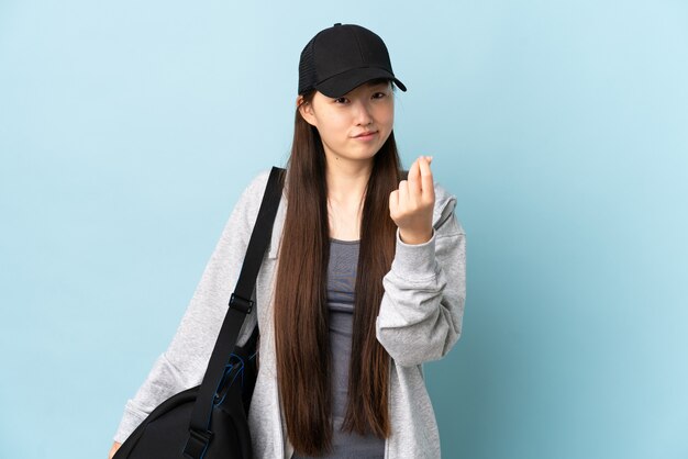 Jonge sport Chinese vrouw met sporttas over geïsoleerd blauw geldgebaar maken