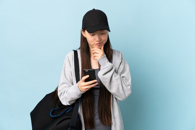 Jonge sport chinese vrouw met sporttas over geïsoleerde blauwe muur die en een bericht denkt verzenden