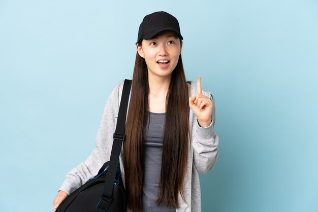 Jonge sport Chinese vrouw met sporttas over geïsoleerde blauwe muur die en verrast benadrukt