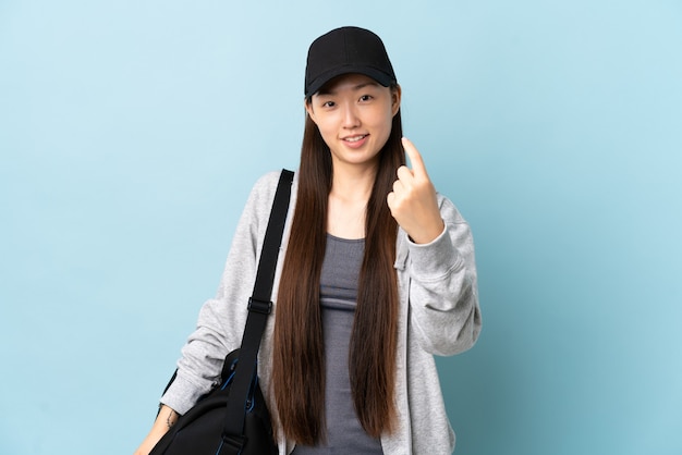 Jonge sport Chinese vrouw met sporttas over geïsoleerde blauwe muur die komend gebaar doet