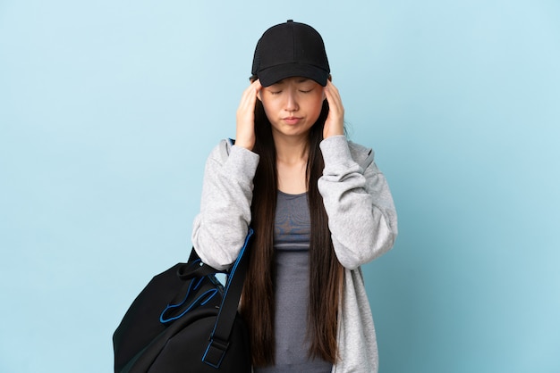 Jonge sport Chinese vrouw met sporttas over geïsoleerde blauwe muur met hoofdpijn