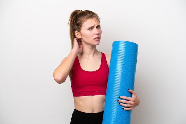 Jonge sport Engelse vrouw die naar yogalessen gaat terwijl ze een mat vasthoudt die op een witte achtergrond wordt geïsoleerd en twijfelt