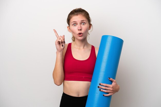 Jonge sport Engelse vrouw die naar yogalessen gaat terwijl ze een mat vasthoudt op een witte achtergrond met de bedoeling de oplossing te realiseren terwijl ze een vinger opheft