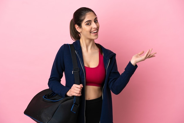 Jonge sport-kaukasische vrouw met sporttas geïsoleerd op een roze achtergrond die de handen naar de zijkant uitstrekt om uit te nodigen om te komen
