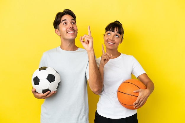 Jonge sport paar voetballen en basketbal geïsoleerd op gele achtergrond wijzend met de wijsvinger een geweldig idee