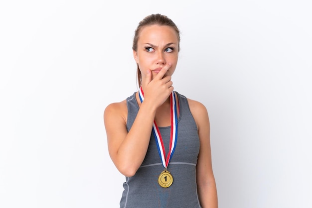 Jonge sport Russisch meisje met medailles geïsoleerd op een witte achtergrond met twijfels en met verwarde gezichtsuitdrukking