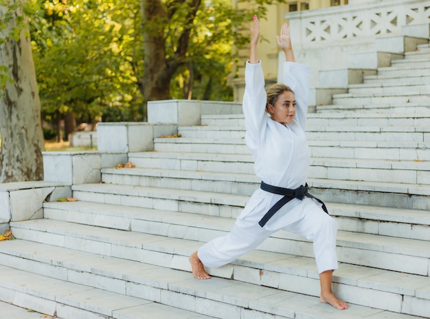 Jonge sport vrouw in een witte kimono met een zwarte band doet een warming-up op de trap voor de training. Vechtsporten, zelfverdediging