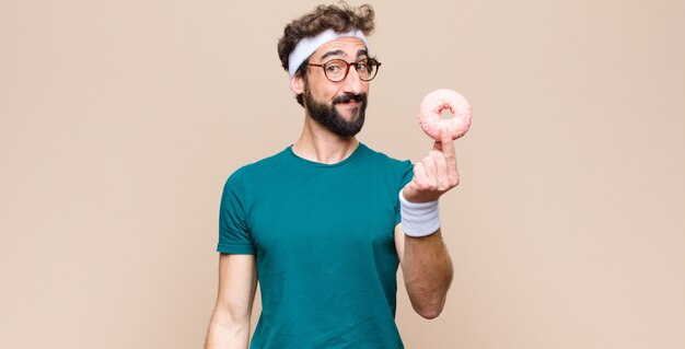 Jonge sportenmens die een snack heeft die een roze suikerdoughnut houdt