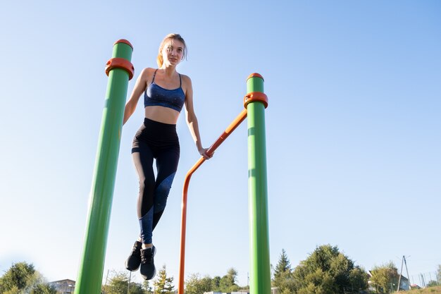 Jonge sportieve atletenvrouw die geschiktheidsoefening op metaalbars in openlucht doen bij stadionhof.