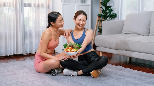 Jonge sportieve Aziatische vrouwen in sportkleding die samen een saladeschaal vasthouden en vullen met levendig fruit en groenten Natuurlijke jeugdige en fit lichaam levensstijl met evenwichtige voeding en lichaamsbeweging thuis Energiek