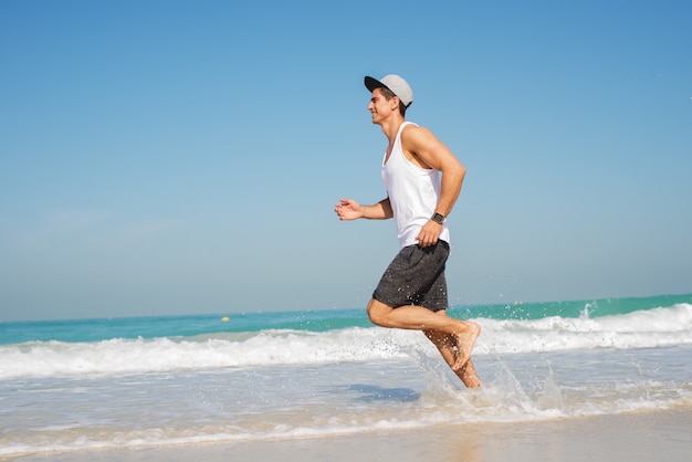 Jonge sportieve man loopt langs het prachtige strand, op zoek gelukkig.