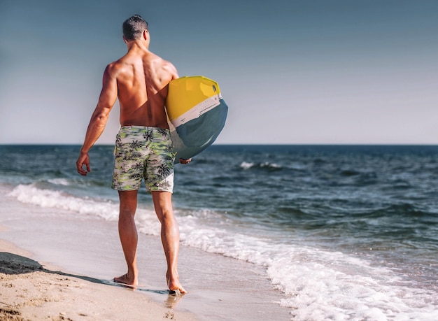 Jonge sportieve man met surfplank door blauw schoon water