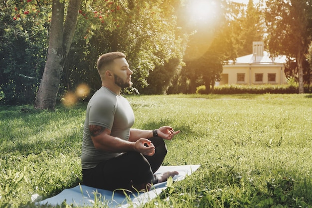 Jonge sportieve man yogi zittend in lotus yoga pose in gras gazon park buitenshuis