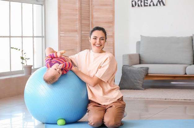 Jonge sportieve moeder en haar baby die thuis oefeningen met fitball doen