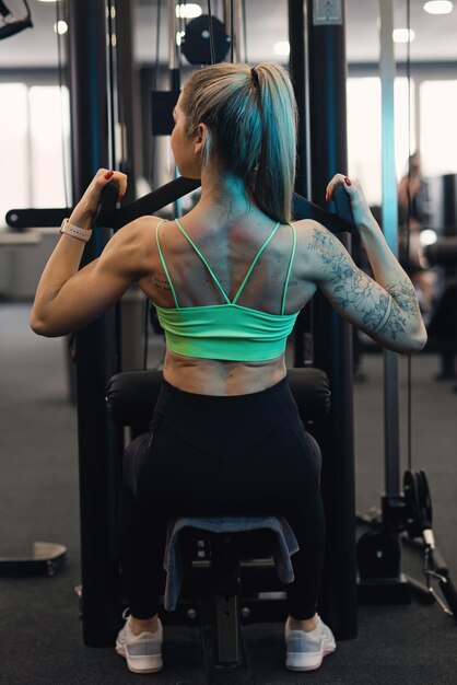 Jonge sportieve vrouw die aan de lat pulldown machine in de sportschool werkt