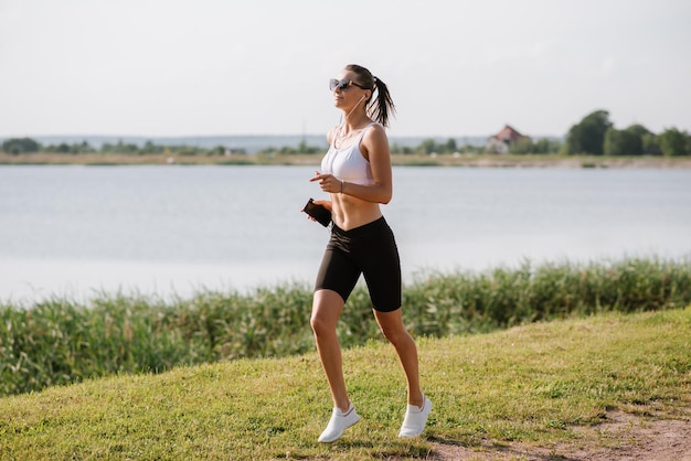 Jonge sportieve vrouw die op een warme zomerdag in het park bij de vijver loopt