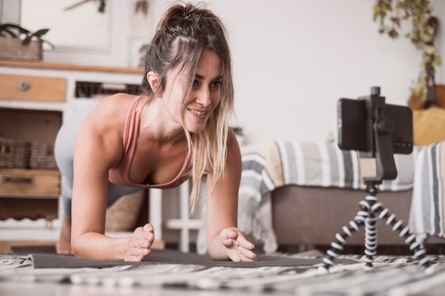 Jonge sportieve vrouw die thuis aan het trainen is, tiener die fitnessoefeningen doet op de vloer van de woonkamer voor het vormen van het lichaam van de billen met behulp van online persoonlijk trainingsprogramma met telefoon, yoga pilates binnenshuis doet