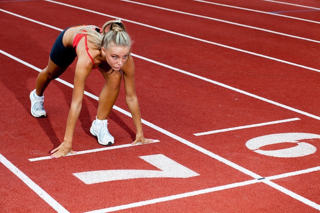 Jonge sportieve vrouw die zich voorbereidt om bij de startlijn te rennen