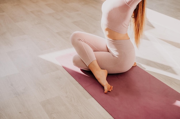 Jonge sportieve vrouw fitness instructeur in roze sportkleding doen stretching en pilates op yoga mat in