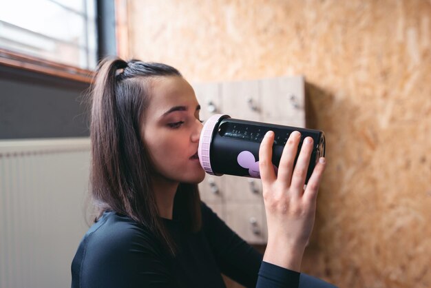 Jonge sportieve vrouw in sportkleding moe, neem een pauze in de sportschool en drink water.