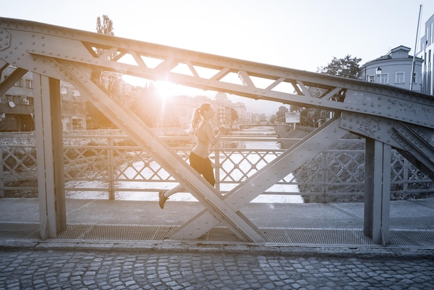 jonge sportieve vrouw joggen over de brug op zonnige ochtend in de stad