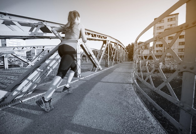 jonge sportieve vrouw joggen over de brug op zonnige ochtend in de stad