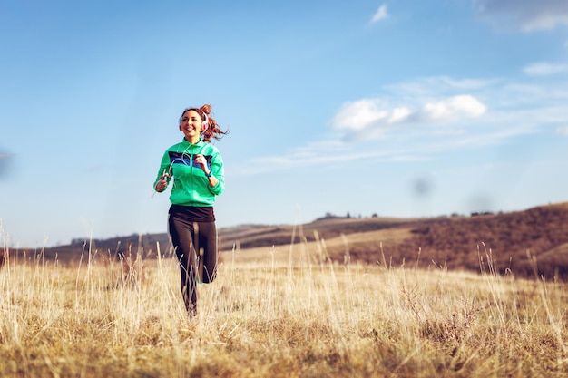 Jonge sportieve vrouw met koptelefoon joggen in de natuur.